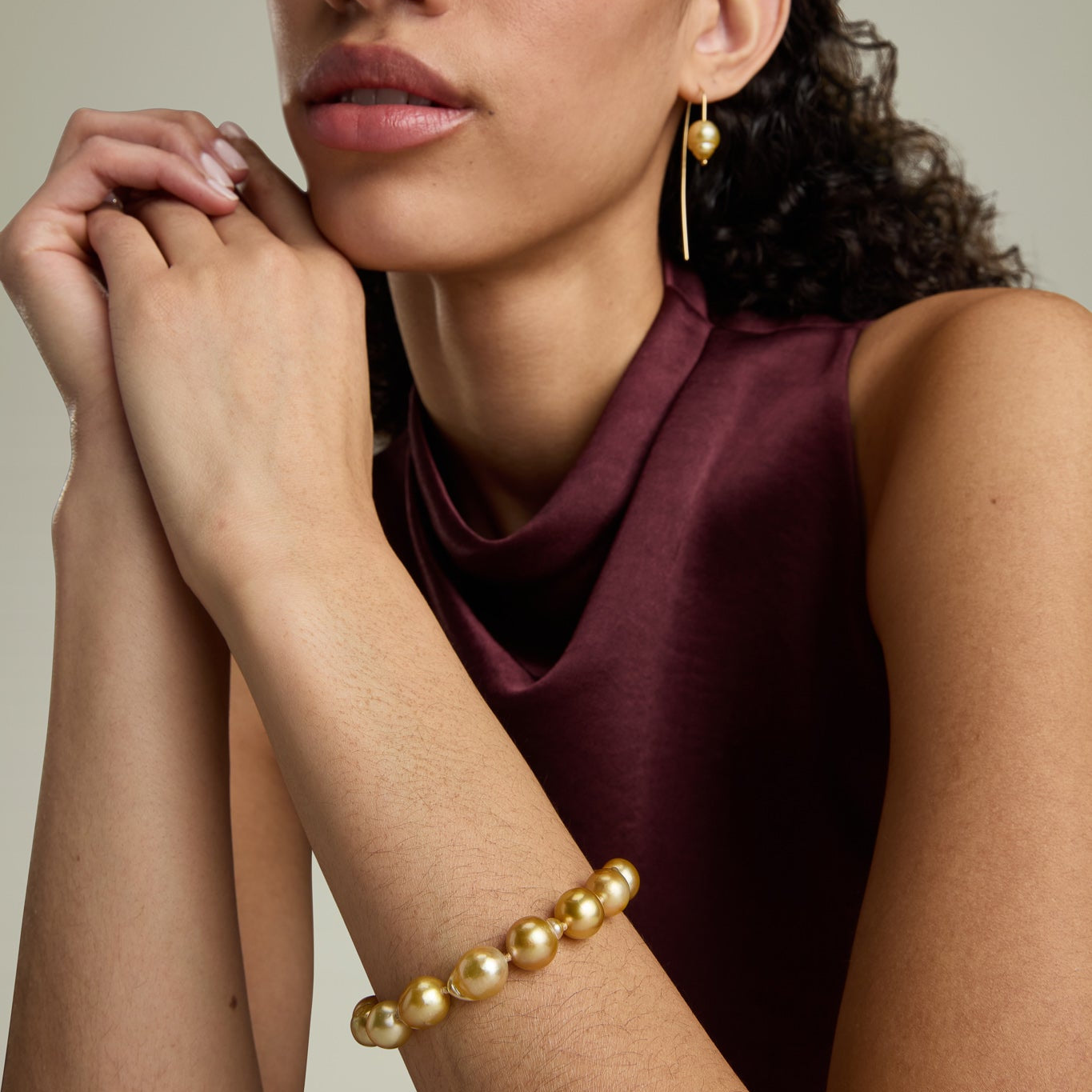 Woman wearing a gold bracelet and earrings against a neutral background